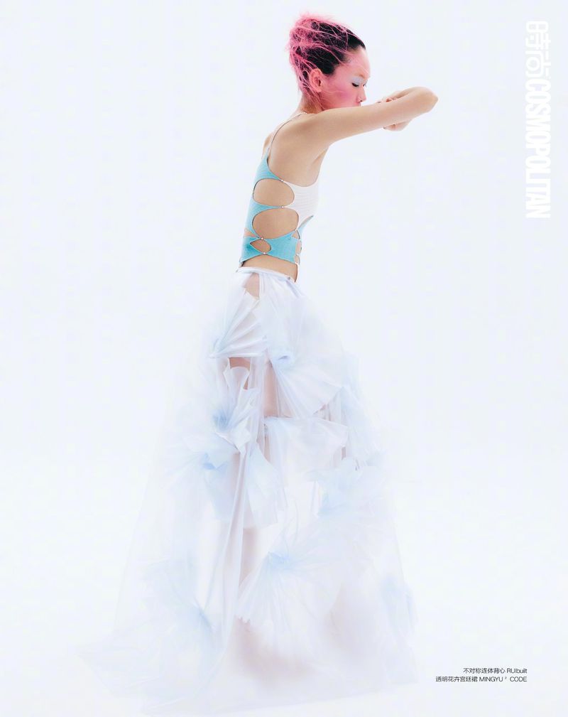 Model Saien Li poses in profile wearing a cutout blue top and layered white tulle skirt against a white studio background.