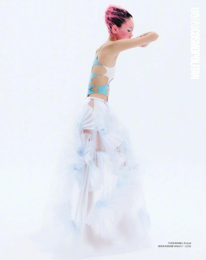 Model Saien Li poses in profile wearing a cutout blue top and layered white tulle skirt against a white studio background.