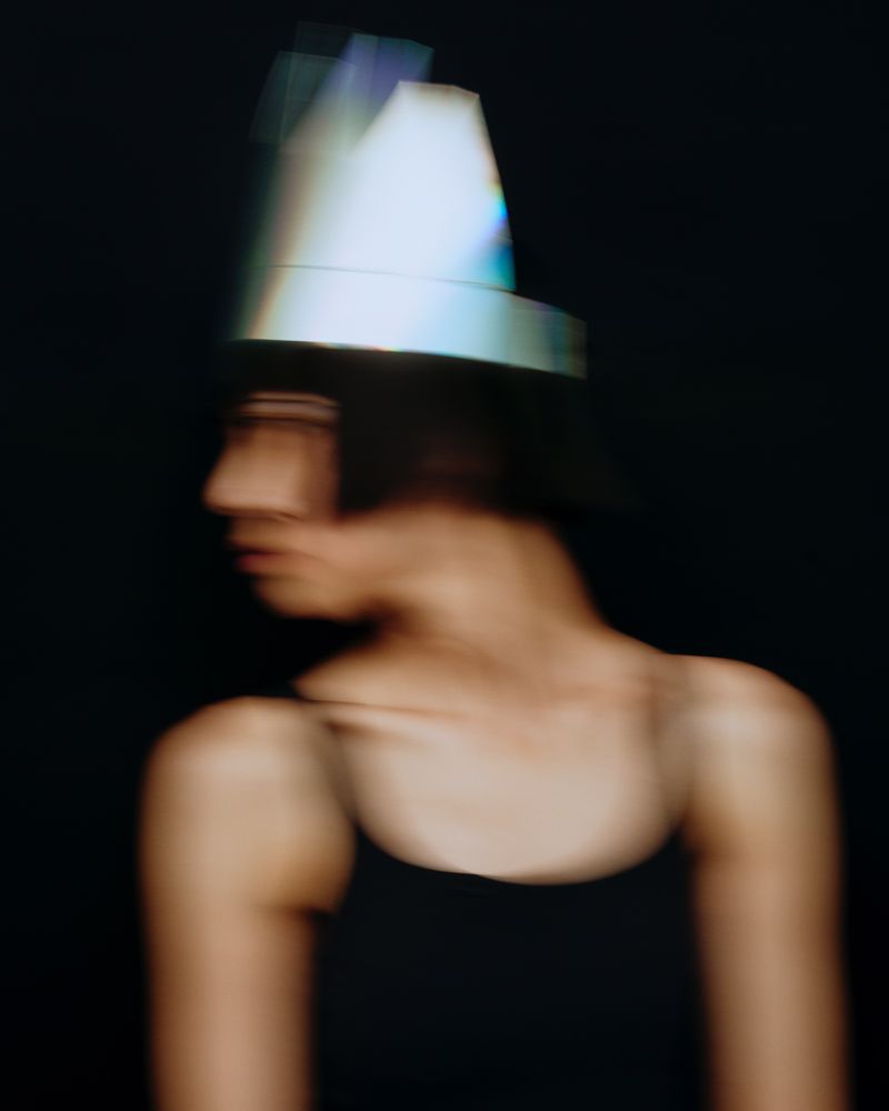 Motion-blurred profile of a model wearing an iridescent sculptural crown headpiece and black top against a dark background.