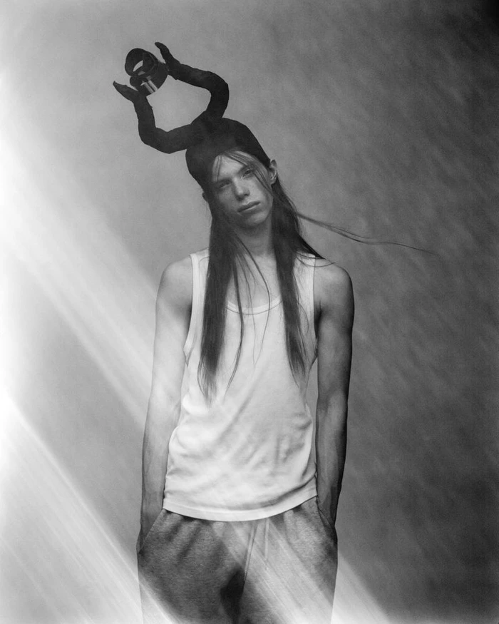 Model with long hair wearing a white tank top and an avant-garde horned headpiece in a black and white portrait.