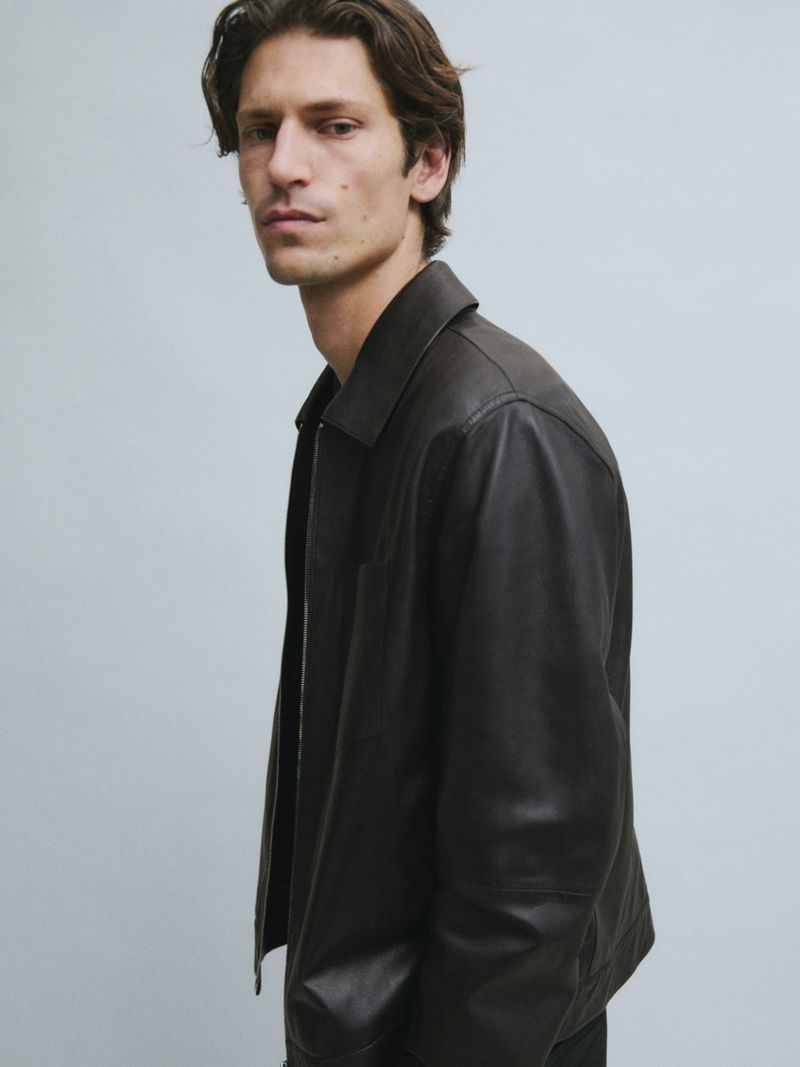 Model Justin Eric Martin wearing a dark leather jacket against a light grey seamless studio background.
