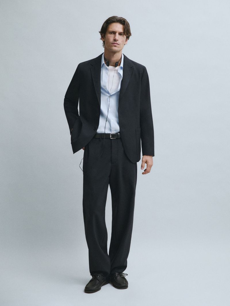 Justin Eric Martin wearing a dark tailored suit and light blue shirt against a grey studio backdrop for Massimo Dutti.
