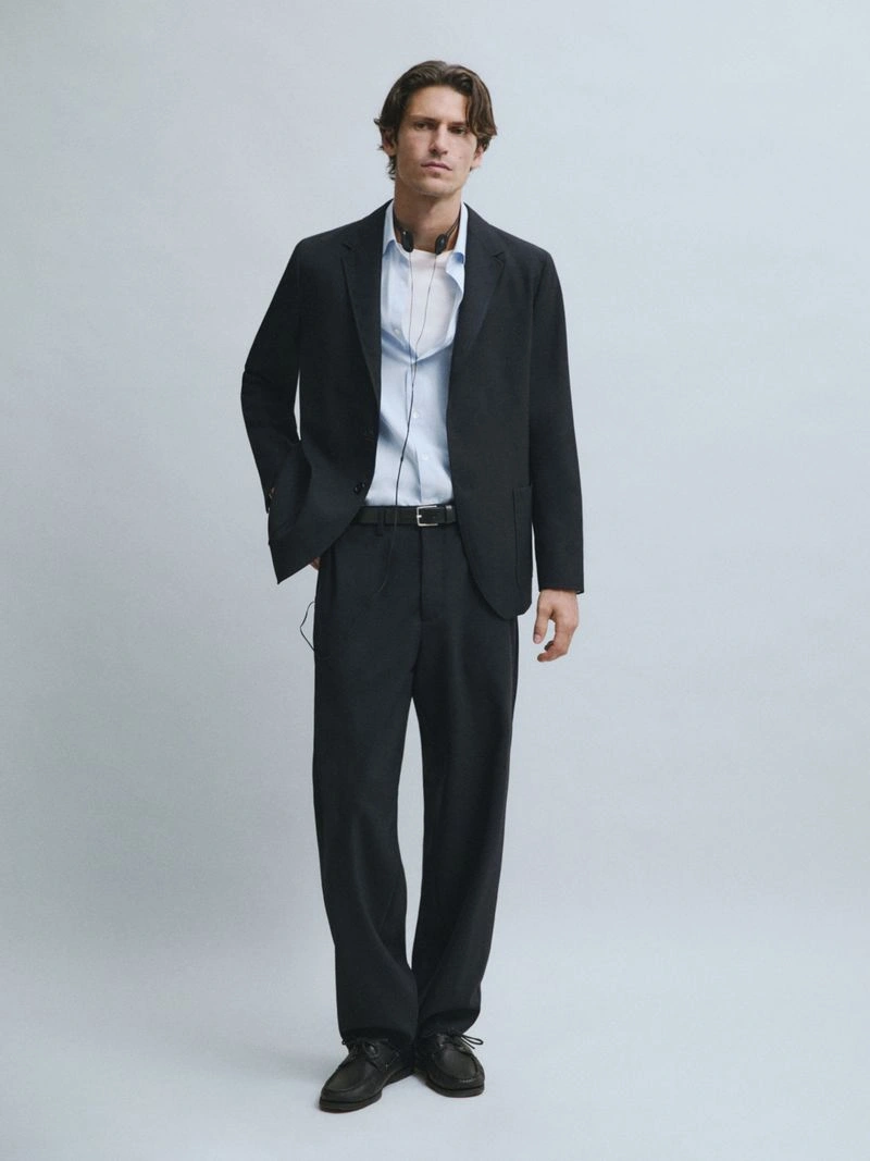 Justin Eric Martin wearing a dark tailored suit and light blue shirt against a grey studio backdrop for Massimo Dutti.