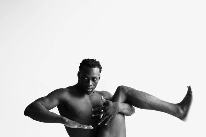 Shirtless Black male dancer striking an expressive, dynamic pose against a plain white studio backdrop.