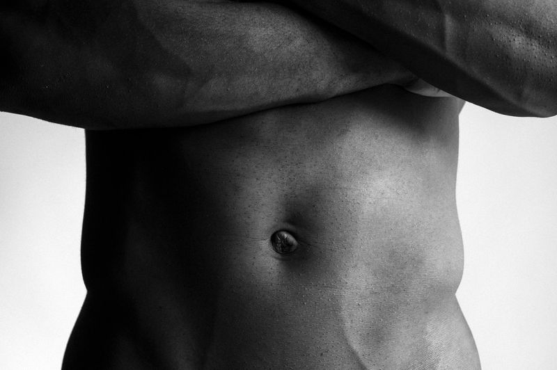 Close-up black and white studio shot of muscular adult male torso with arms crossed, emphasizing fitness and body aesthetics.
