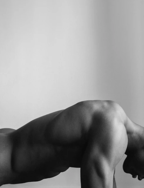 Black and white close-up of a muscular adult man's torso and back in a bent-over pose against a light background in a photo studio.