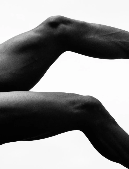 Monochrome studio shot of two bent human legs, highlighting muscular detail and form against a stark white background.