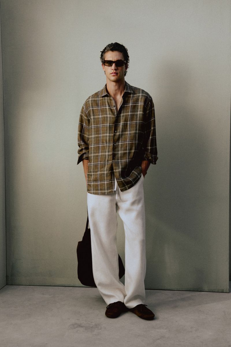 Model Francisco Henriques wearing a plaid button-up shirt, loose white trousers, and dark sunglasses for a Massimo Dutti lookbook.