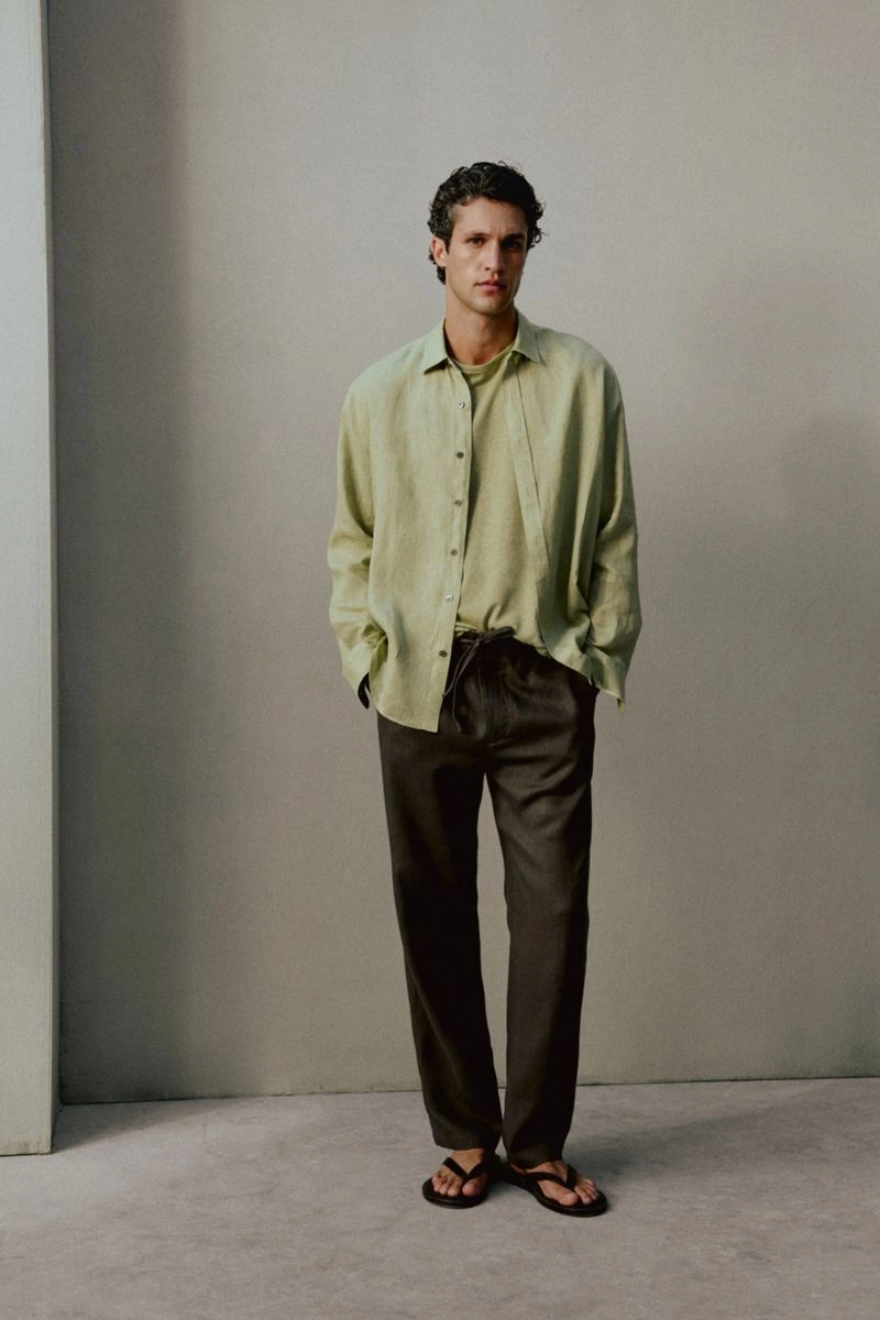 Model Francisco Henriques wearing a light sage shirt and dark relaxed trousers against a neutral grey studio backdrop.