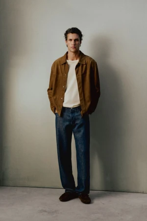 Model Francisco Henriques wearing a brown jacket, white t-shirt, and dark blue jeans against a neutral studio wall.