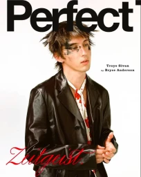 Troye Sivan wearing a black leather jacket and patterned neck scarf against a white studio background on a magazine cover.