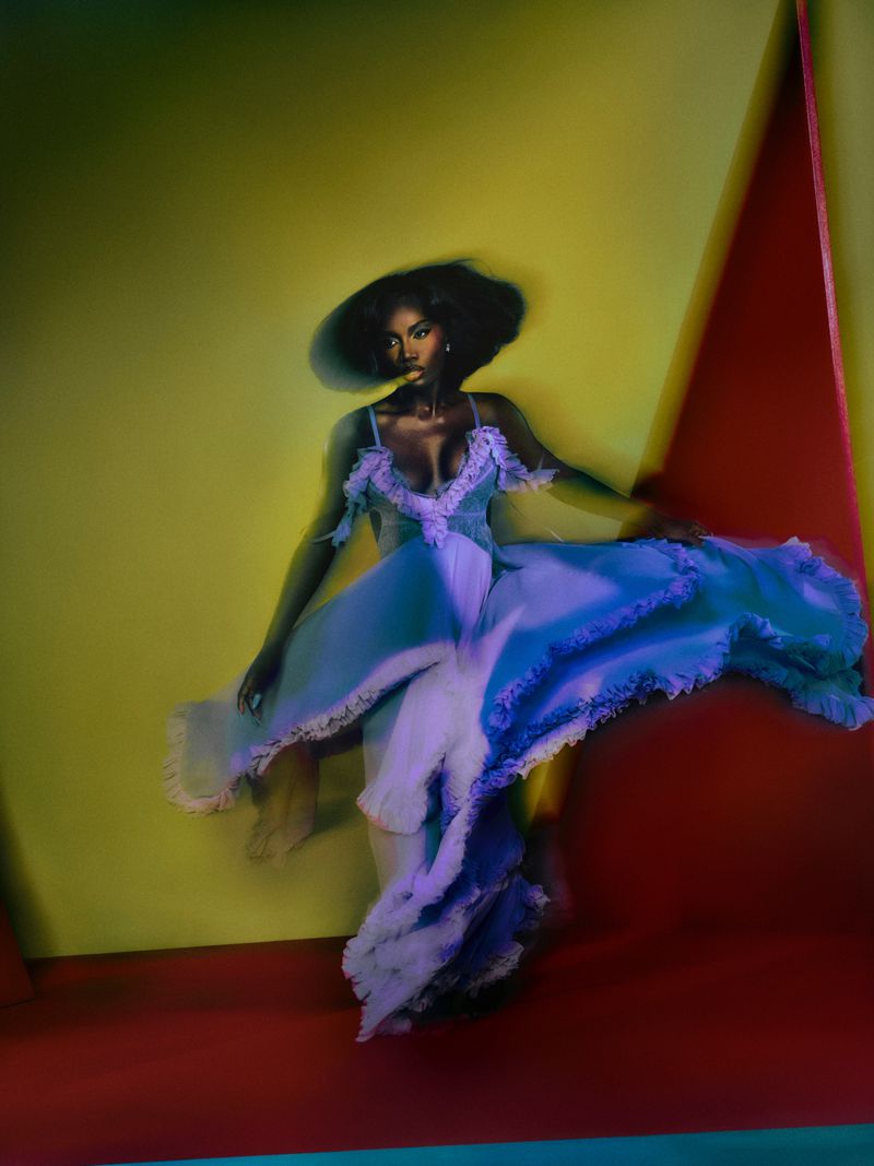 Elegant black woman in a light blue gown and large sunhat poses in a photo studio setting, motion blur adds a dynamic feel to the image.