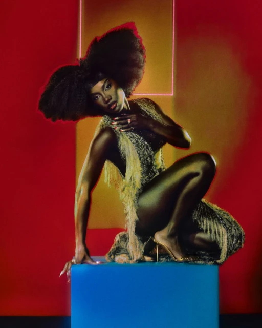 Elegant Black woman with large afro hairstyle poses on a blue cube in a feathered dress against a red studio backdrop with neon square.
