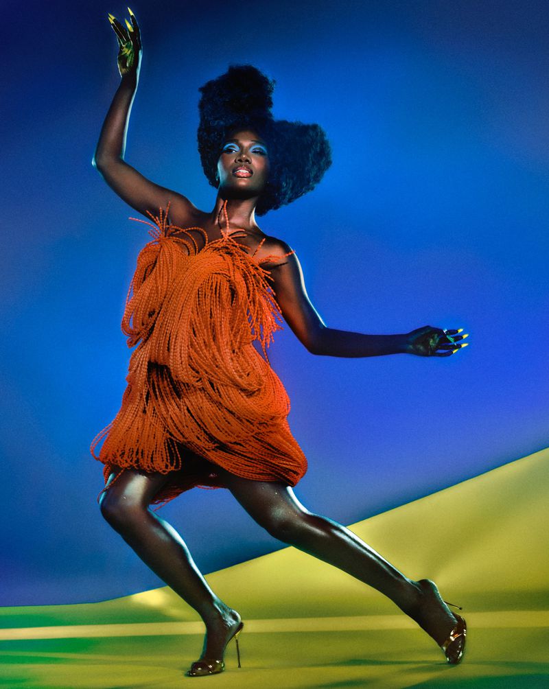 Fashionable African-American woman in a fringed orange mini dress strikes a pose in a dynamic studio shot with blue-and-yellow backdrop.