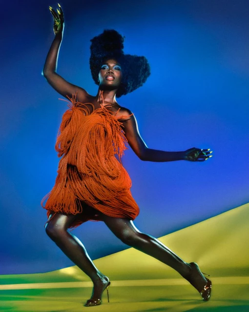 Fashionable African-American woman in a fringed orange mini dress strikes a pose in a dynamic studio shot with blue-and-yellow backdrop.