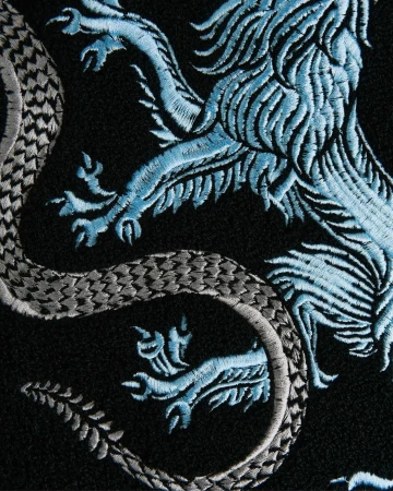 Close-up of intricate light blue and silver embroidered heraldic lion crest on black textile.