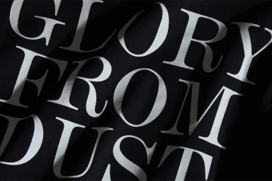 Close-up of white serif text reading Glory From Dust printed on folded black fabric.