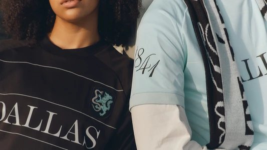 Cropped shot of two models wearing black and light blue Atlético Dallas soccer jerseys with custom crest and typography.
