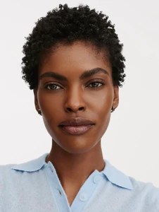 Beauty portrait of model Amilna Estevao with short natural curls wearing a powder blue knit polo against a plain white background.