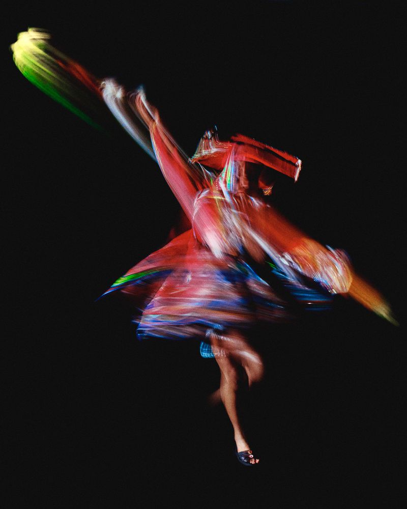 Abstract long-exposure photography of a woman in motion wearing a dress against a black background, creating a dynamic and artistic effect.