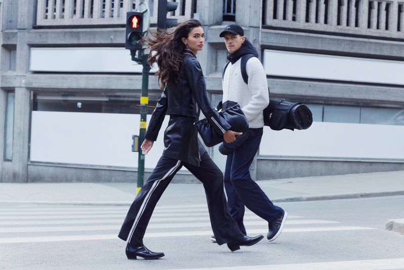 A woman in a black leather jacket and a man in a white fleece jacket walking across a pedestrian crosswalk in an urban city setting.