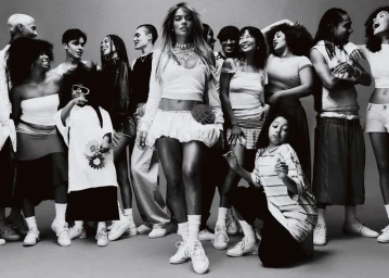 Karol G stands centered among a diverse group of people in streetwear and sneakers against a seamless studio backdrop.