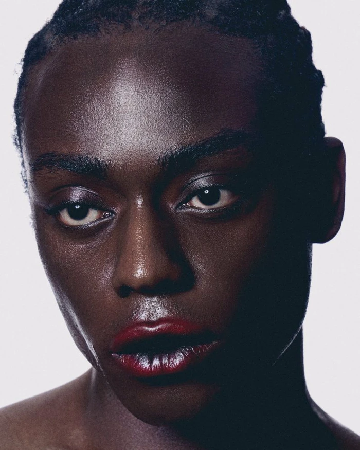 Close-up portrait of a Black model with glossy red lipstick against a bright white seamless background.