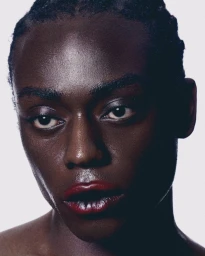 Close-up portrait of a Black model with glossy red lipstick against a bright white seamless background.