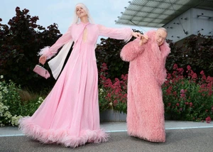 Eva Herzigova in a pink feather-trimmed gown posing alongside Walter Pfeiffer in an oversized pink shaggy coat outdoors.
