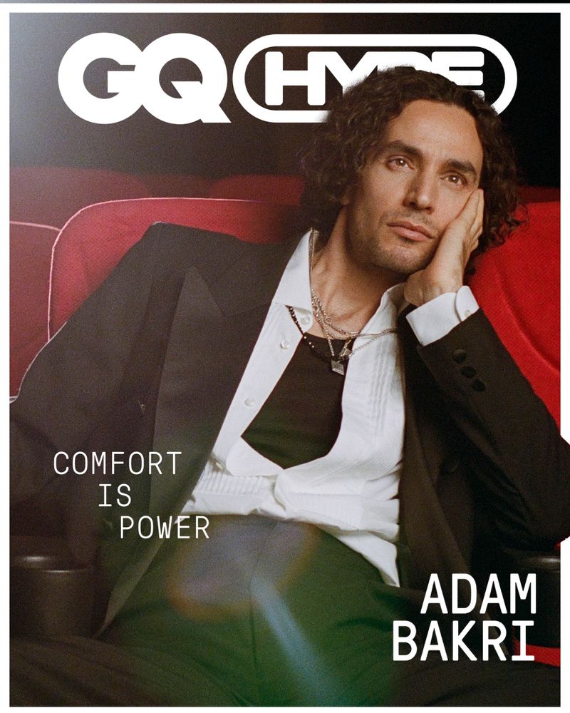 Adam Bakri sitting in a red cinema seat, wearing a white shirt and black blazer, with the GQ Hype logo and text overlaying the image.