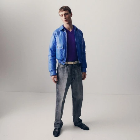 Model Clement Chabernaud wearing a blue cropped jacket, purple knit, and grey wash jeans against a white seamless background.