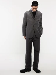 Model Xiangyu Li wearing a grey tailored suit jacket, matching trousers, and black dress shoes against a white studio background.