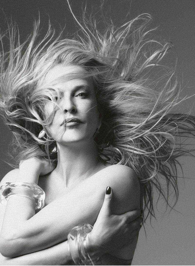 Black and white portrait of model Karen Mulder with windblown hair, crossing her arms while wearing clear chunky bangles.
