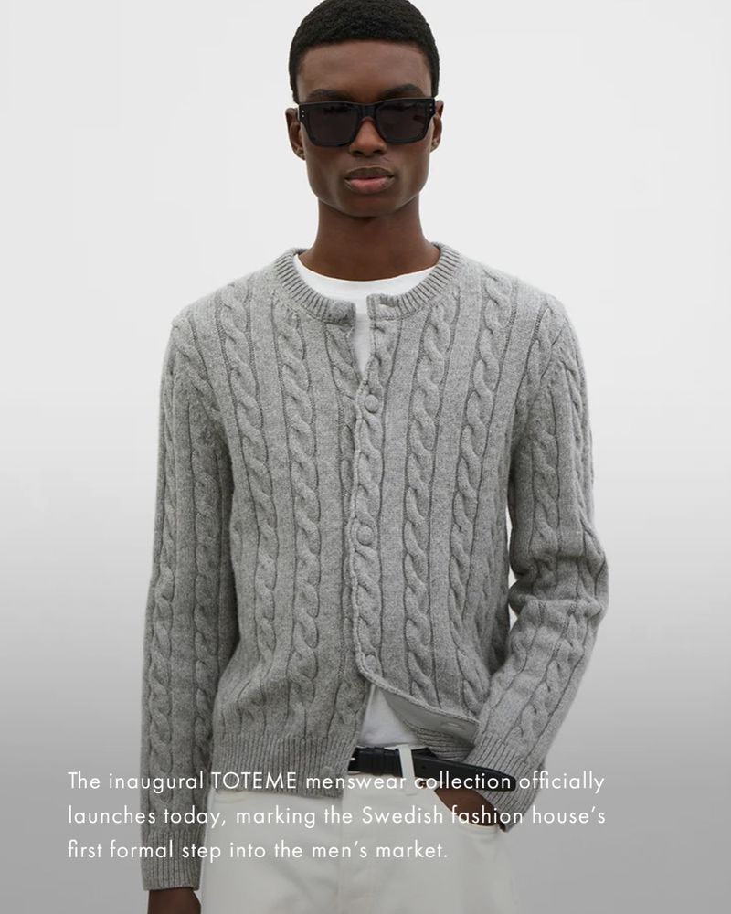 Model wearing dark sunglasses and a grey cable-knit cardigan over a white shirt against a neutral grey studio backdrop.