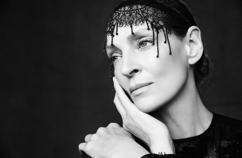 Black and white portrait of a woman with lace head covering, resting her face on her hands against a dark, blurred background.