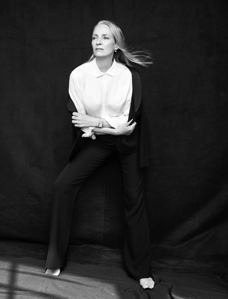 Black and white studio portrait of an adult woman with long hair wearing a white shirt, dark trousers, and a blazer draped over her shoulders.