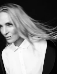 Portrait of Uma Thurman with long blonde hair in motion wearing a white collared shirt against a dark background