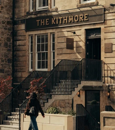 A person walking past the sandstone facade and black staircase entrance of The Kithmore hotel.