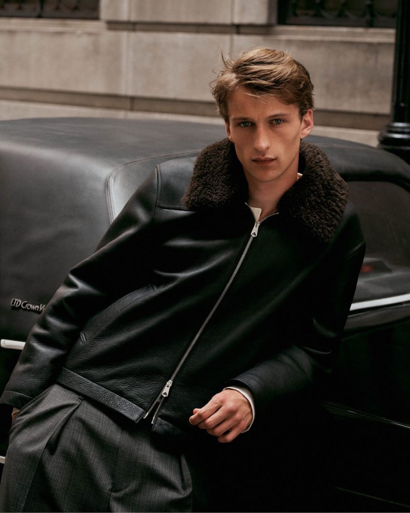 Model Vasko Luyckx in a black shearling-collar leather jacket leaning on a vintage car for Paul Smith.