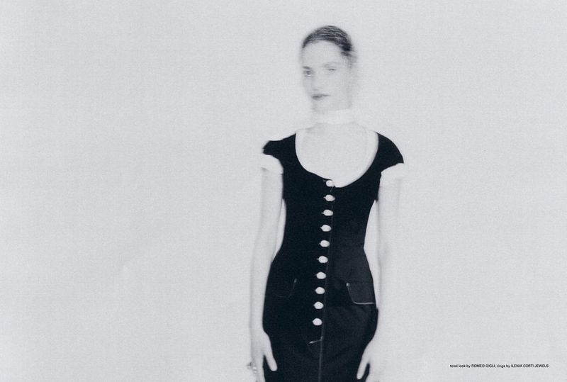 Monochromatic fashion portrait of a woman wearing a black dress with white buttons in a photo studio setting. Soft focus aesthetic.