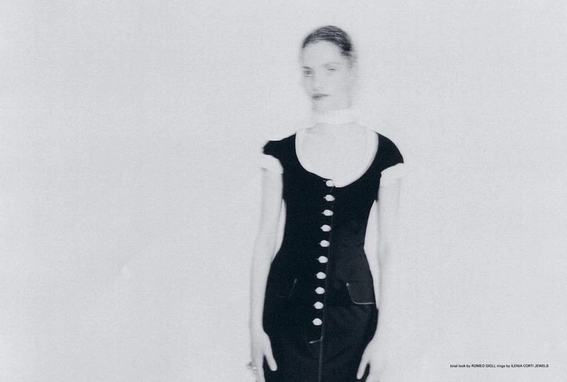 Monochromatic fashion portrait of a woman wearing a black dress with white buttons in a photo studio setting. Soft focus aesthetic.