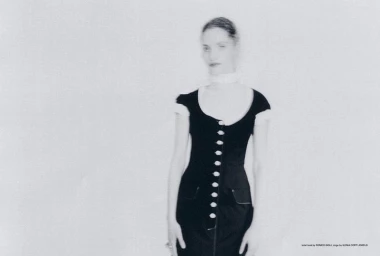 Julia Kuźniar wearing a fitted black button-front dress in a high-key monochrome studio portrait.