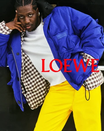 Lil Yachty posing in a bright blue Loewe jacket with gingham lining, a white crewneck, and vibrant yellow trousers.