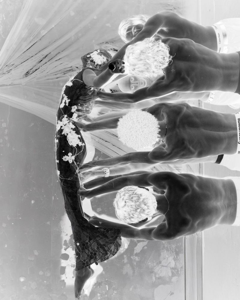 Monochromatic fashion shot features woman in ornate gown, assisted by four men. Negative effect and studio lighting create a striking visual.