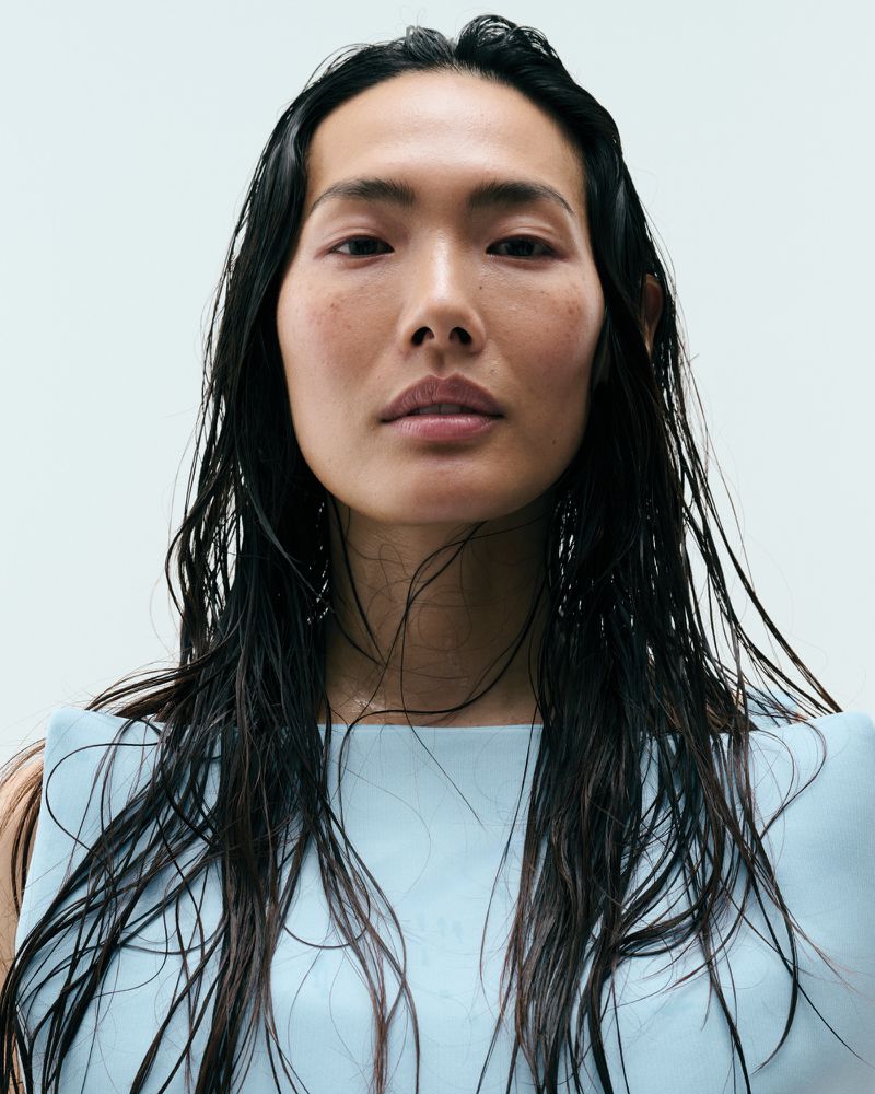Beauty portrait of model Chinchin Hsu with long wet dark hair wearing a powder blue structured top against a pale seamless backdrop.