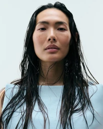 Beauty portrait of model Chinchin Hsu with long wet dark hair wearing a powder blue structured top against a pale seamless backdrop.