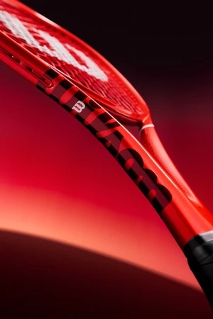 Close-up angled view of a glossy red Wilson tennis racket against a graduated red and black background.
