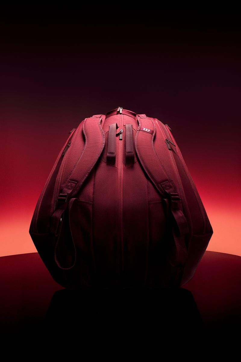 Burgundy Wilson sports backpack standing on a reflective surface against a glowing red and orange gradient backdrop.