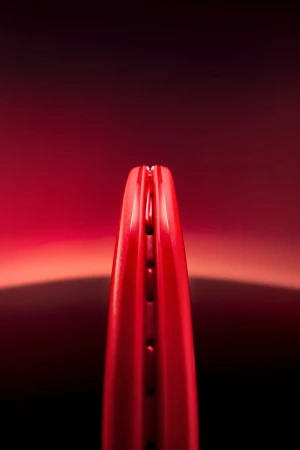 Close-up detail of a glossy red tennis racket rim and grommet strip centered against a dark red gradient background.