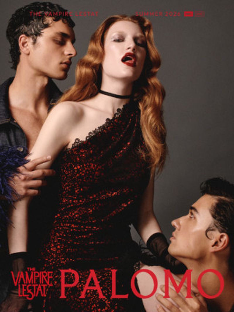 Red-haired woman in a black and red lace dress flanked by two male models against a studio backdrop for Palomo Spain.